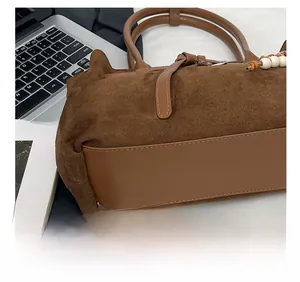 Close-up of fine stitching on a brown suede tote bag with leather trim and bead detail