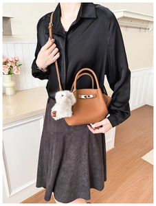 Detail of brown litchi pattern leather bucket bag with metal lock and plush bunny charm