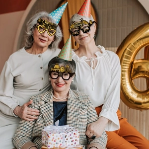 Three elegant senior women wearing glittery gold and black 60th birthday party glasses