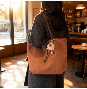 Detailed view of brown suede tote bag with plush lamb charm and leather straps