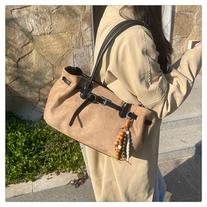 Close-up of brown suede tote bag featuring black leather straps and ethnic bead charm