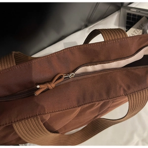 Detail of a brown tote bag featuring a durable zipper closure and woven handle straps