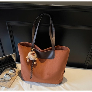 Detail of suede tote bag with leather trim and plush charm on a workspace background