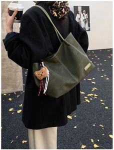 Dark green large tote bag with brown bear charm shown in a city street setting