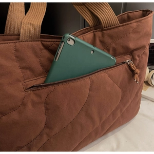 Detail of wave quilted brown tote bag showing a front zipper pocket with a tablet inside