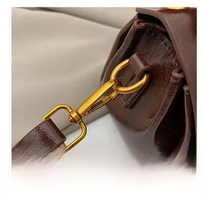 Close-up of vintage gold metal swivel hook and stitching on dark brown leather strap