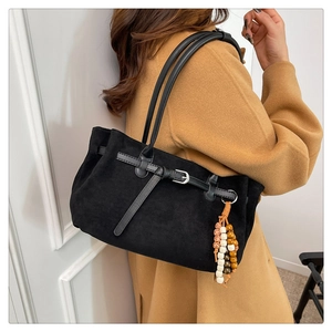 Detail of black suede tote bag featuring decorative straps and a colorful beaded tassel
