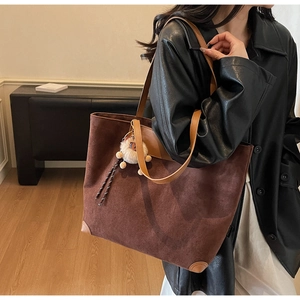 Detail of vintage brown suede tote bag featuring leather trim and decorative fur ball charm