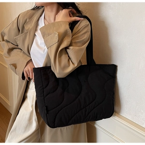 Close-up of black quilted tote bag with wave pattern stitching shown on shoulder