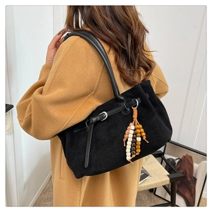 Detail of black suede tote bag with wooden bead charm on a camel-coated model shoulder