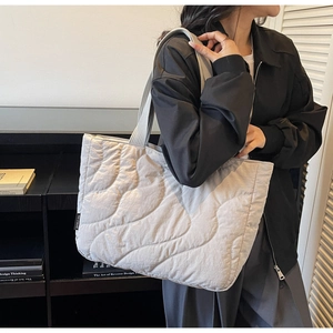Detailed view of grey quilted tote bag with wavy stitching and brand label on shoulder