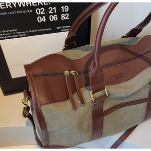 Detailed close-up of army green canvas travel duffle bag with brown leather trim and metal zipper