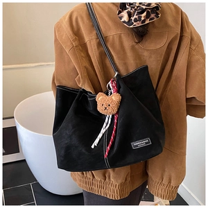 Detail of black tote bag with white stitching, plush bear charm and woven rope accent