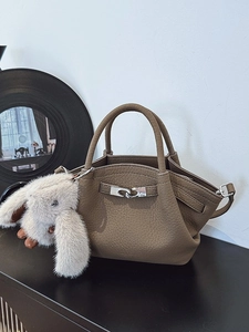 Dark brown lychee leather handbag with silver lock and plush bunny charm on black surface