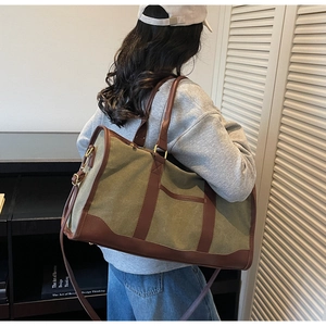Detail of olive canvas travel bag featuring brown leather straps and adjustable shoulder hook