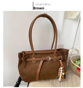 Detail of a brown suede tote bag with leather straps and decorative beaded tassel