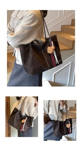 Detail of a brown leather tote bag with contrast stitching and teddy bear charm accessory
