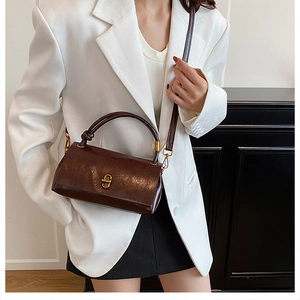 Detail of dark brown leather handbag featuring a gold metal twist lock and knotted handle