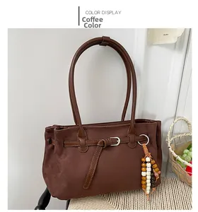 Brown suede tote bag detail featuring a decorative buckle and beaded pendant on a chair