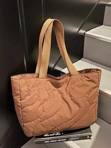Stylish brown quilted puffer tote bag for women with wave stitching on a city step