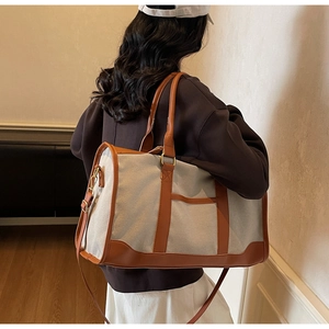 Detail of large canvas travel tote bag with brown leather trim carried by a model