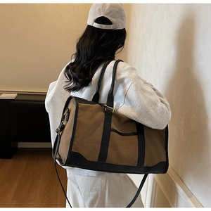 Detail of a large canvas travel bag with leather straps worn by a model in a modern room