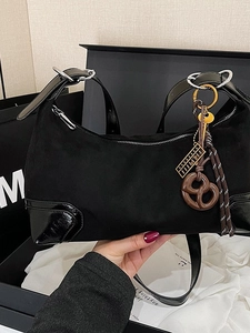 Borsa a tracolla nera opaca con bordi lucidi e ciondoli su sfondo di scatola regalo
