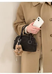 Dettaglio borsa bowling in camoscio grigio scuro con cuciture bianche e ciondolo a orsetto