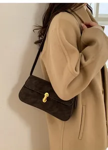 Sac sous le bras en suédine marron avec fermoir doré porté avec un manteau camel