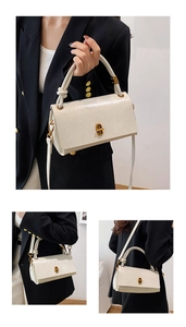 Detail view of cream leather handbag with gold twist lock and adjustable shoulder strap