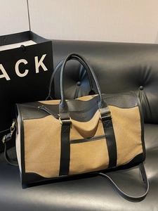 Large khaki canvas travel bag with black leather trim on a vintage leather sofa