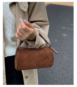 Detailed view of a brown suede cylinder bag held by a model on a street background