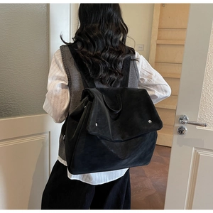 Rear view of a model wearing a large black frosted backpack with flap and metal snaps
