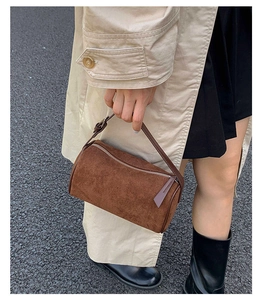 Detailed view of a brown suede cylinder handbag with silver zipper and leather handle