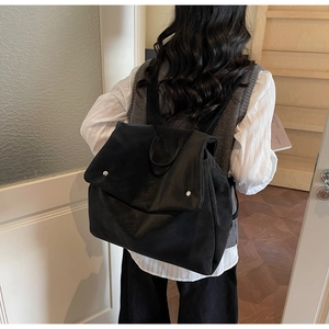 Detail of matte black backpack showing wide flap with silver cylindrical snap closures