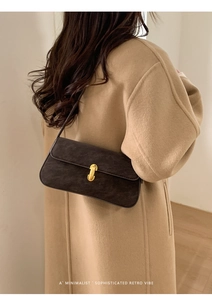 Détail d'un sac bandoulière en daim avec fermoir en U doré sur un manteau en laine