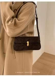 Détail d'un sac à bandoulière en daim marron foncé avec boucle dorée sur un manteau