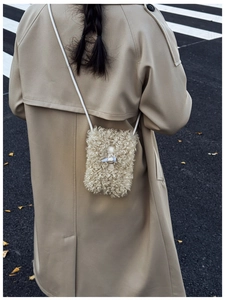 Close-up of cream fuzzy crossbody bag with horn buckle on beige trench coat outfit
