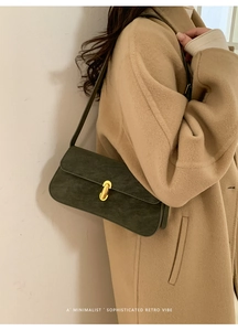 Détail du sac baguette rétro vert foncé avec boucle dorée sur un manteau en laine beige