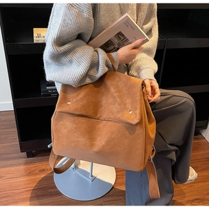 Detail of caramel brown suede backpack featuring silver rivets and a minimalist flap design