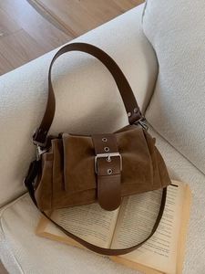 Sac bandoulière vintage en daim marron foncé avec large boucle sur canapé blanc
