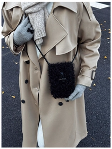Detail of black fuzzy faux fur crossbody bucket bag with toggles on a winter street