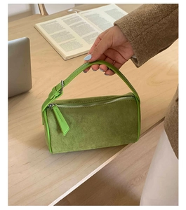 Close-up of a green suede cylinder pillow bag with silver zipper and leather handle