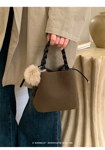 Minimalist brown bucket bag with woven handle and pompom charm in a lifestyle setting