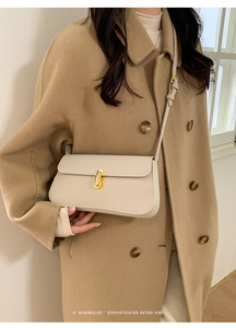 Détail du sac à bandoulière crème minimaliste avec fermoir doré sur manteau