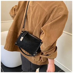 Detail of vintage horseshoe gold buckle and white stitching on black leather crossbody bag