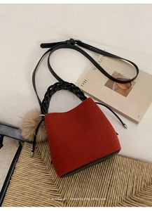 Close-up of red corduroy bucket bag with woven handle and plush pom-pom charm