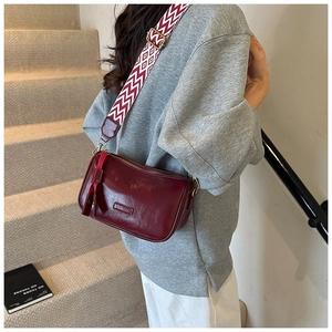 Detail of burgundy leather Boston bag with a wide geometric diamond strap and tassel charm