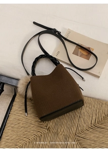 Close-up of brown twill bucket bag with black leather base and a beige fur ball charm