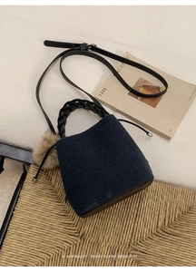 Detail of navy blue felt bucket bag featuring woven handle and pompom charm detail